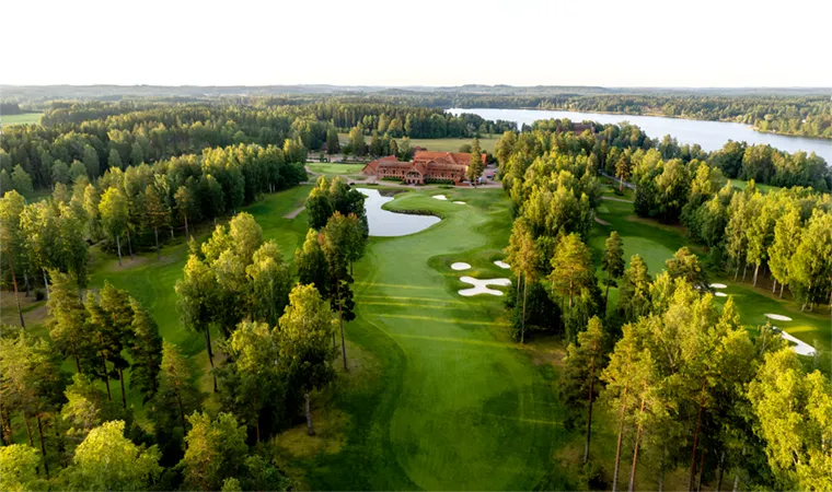 Luftaufnahme eines malerischen, von dichten Bäumen umgebenen Golfplatzes mit Sandbunkern, grünen Fairways, einem Clubhaus und einem See im Hintergrund - die perfekte Inspiration für Ihre nächste Golfrundreise durch Irland unter freiem Himmel.