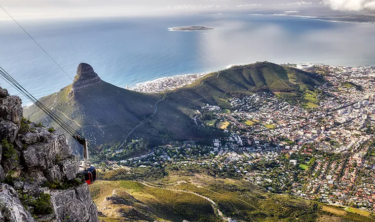 Ein malerischer Blick vom Tafelberg auf Ihrer Golfreise Südafrika, der eine Seilbahn, einen kegelförmigen Hügel, die Stadt darunter und die Kapstadt mit dem Meer und einer kleinen Insel in der Ferne zeigt.
